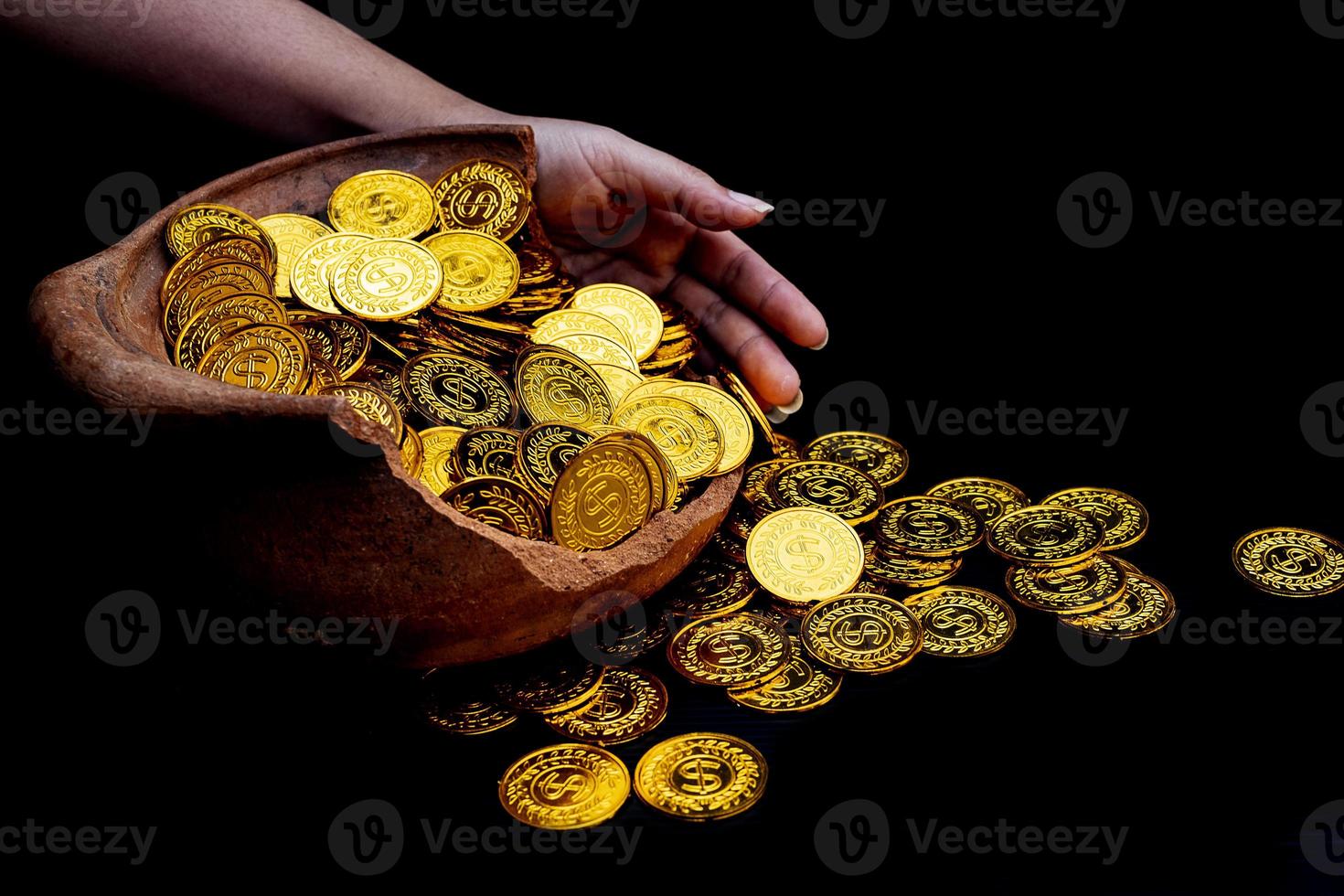 Moneda de oro en la mano en lotes apilando monedas de oro en el frasco del tesoro roto fondo blanco foto