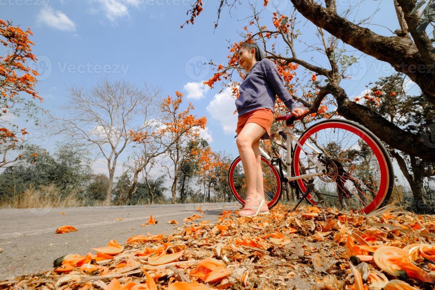 Mujer de pie junto a su bicicleta al aire libre en el árbol de palash con un fondo lleno de hermosas flores de naranja foto