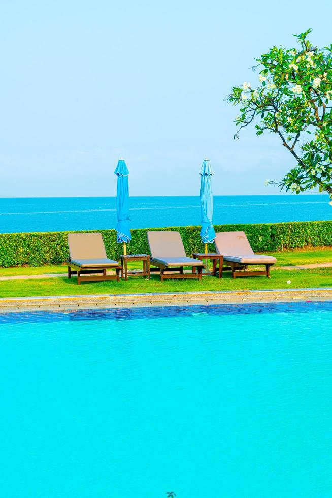 Piscina de sillas o camas y sombrillas alrededor de la piscina con fondo de mar - vacaciones y concepto de vacaciones foto