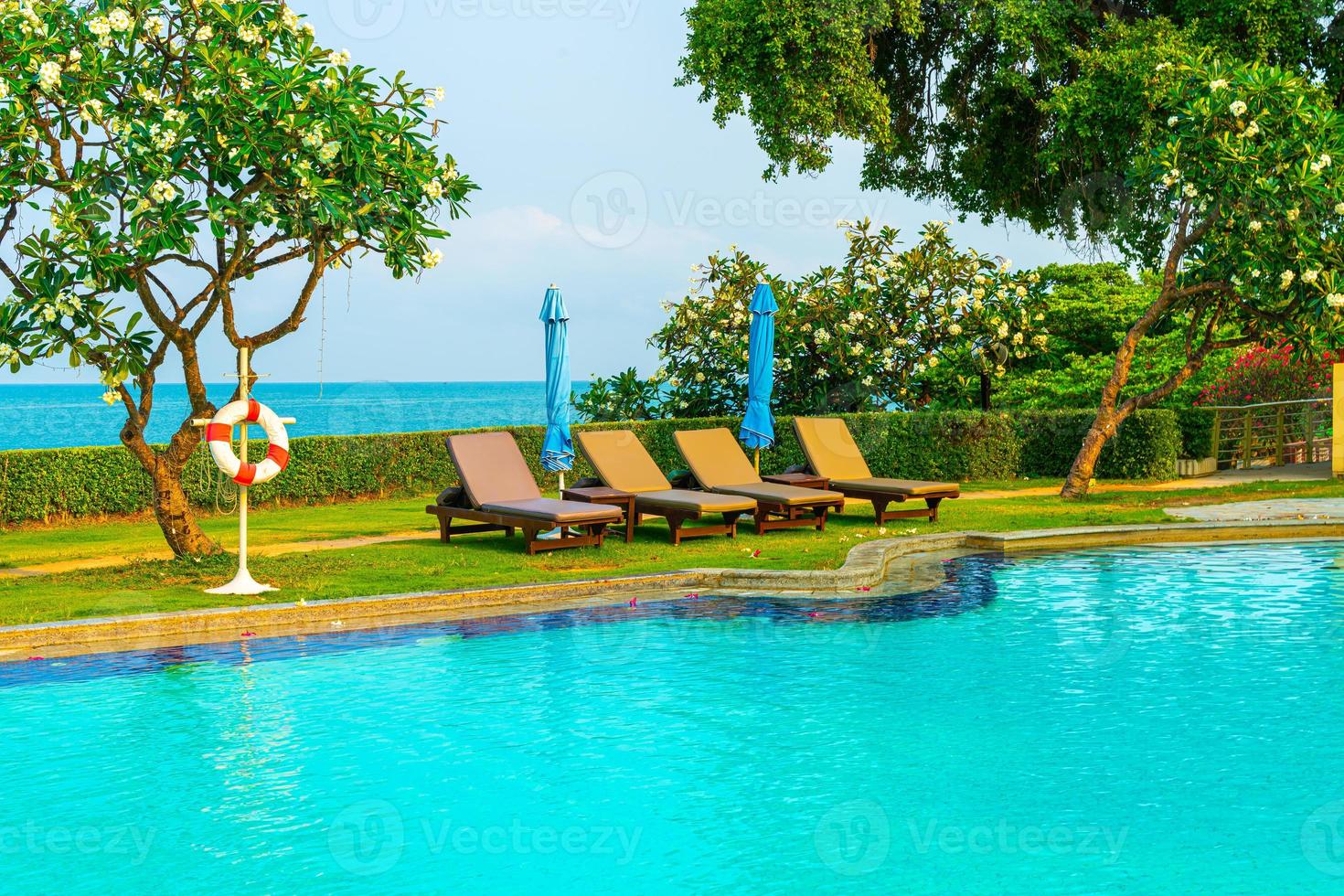 Chair pools or beds and umbrellas around swimming pool with sea background - Holidays and vacation concept photo