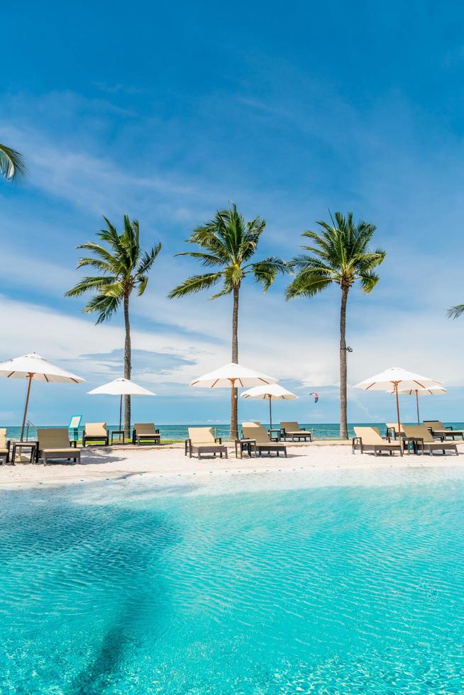 Chair pools or beds and umbrellas around swimming pool with sea background - Holidays and vacation concept photo