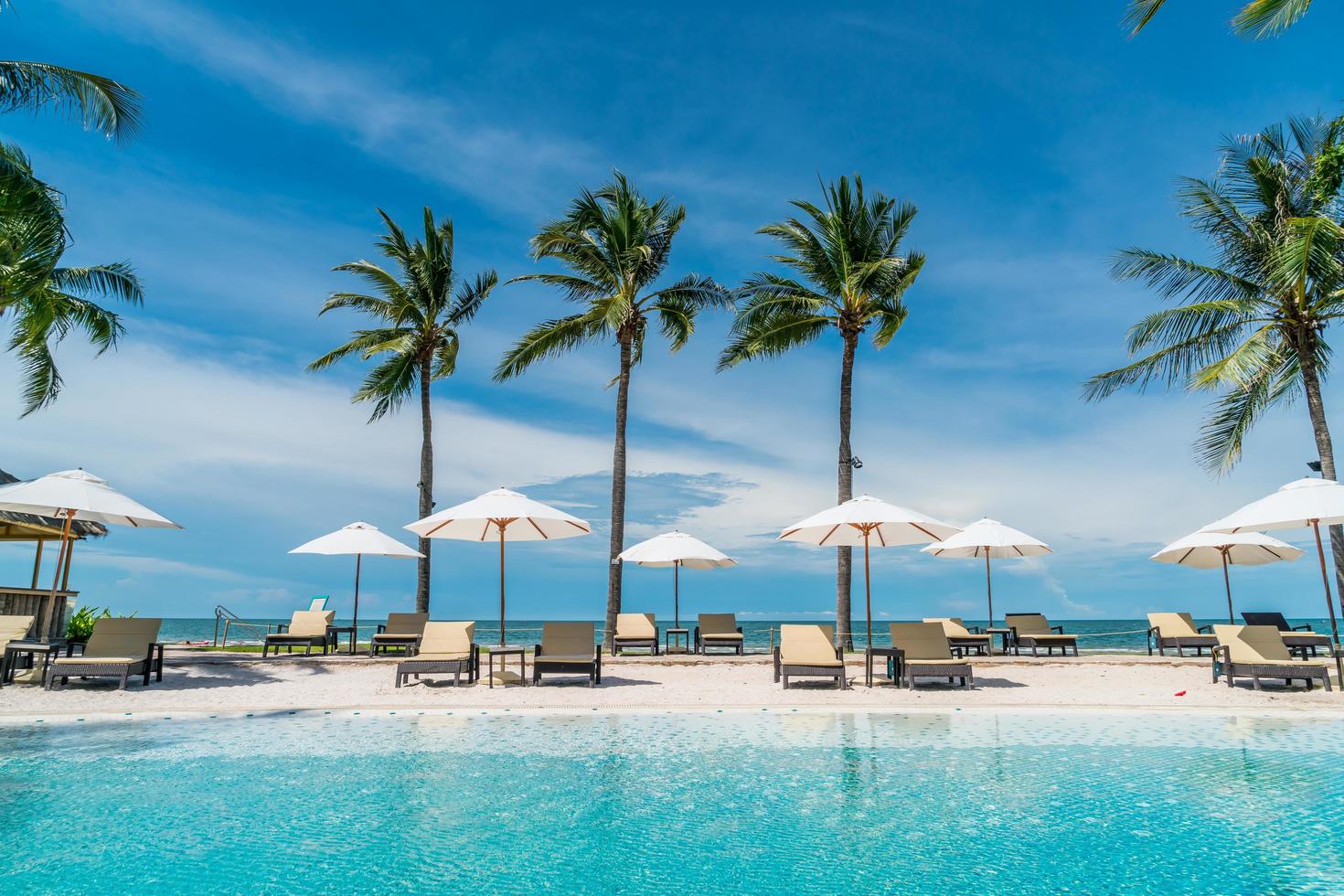 Chair pools or beds and umbrellas around swimming pool with sea background - Holidays and vacation concept photo