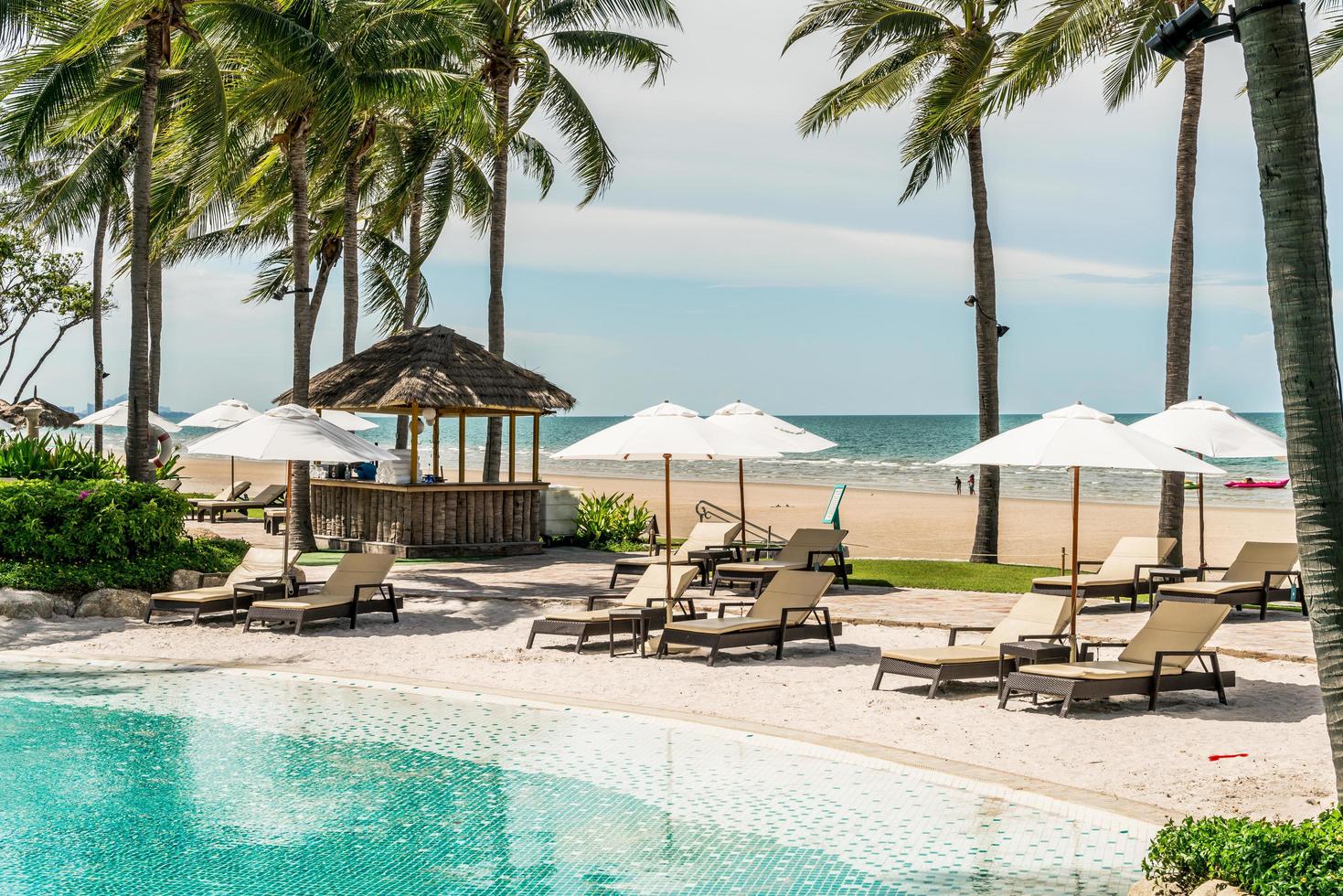 Chair pools or beds and umbrellas around swimming pool with sea background - Holidays and vacation concept photo