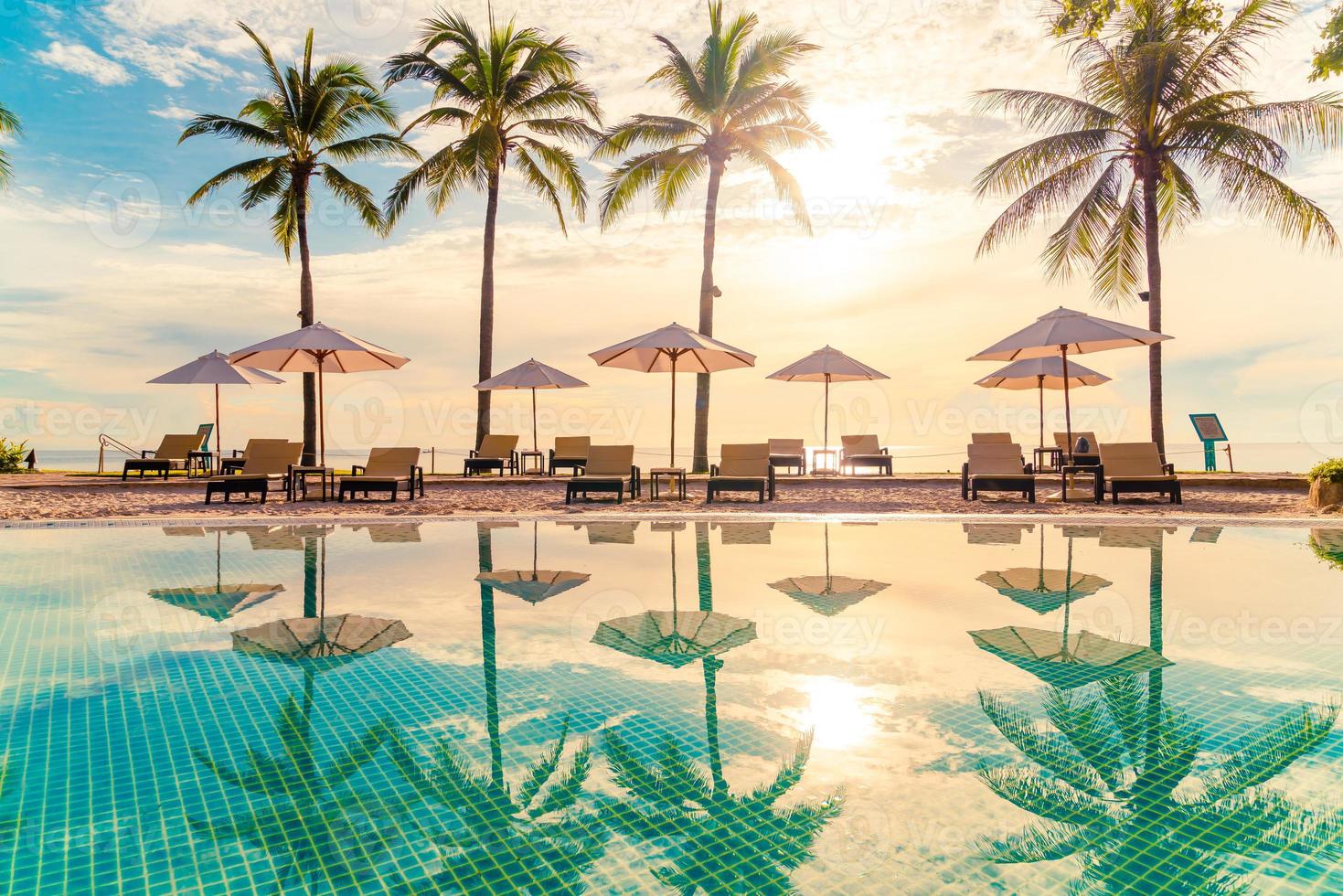 Beautiful luxury umbrellas and chairs around an outdoor swimming pool in hotel and resort with coconut palm trees on sunset or sunrise sky - holiday and vacation concept photo