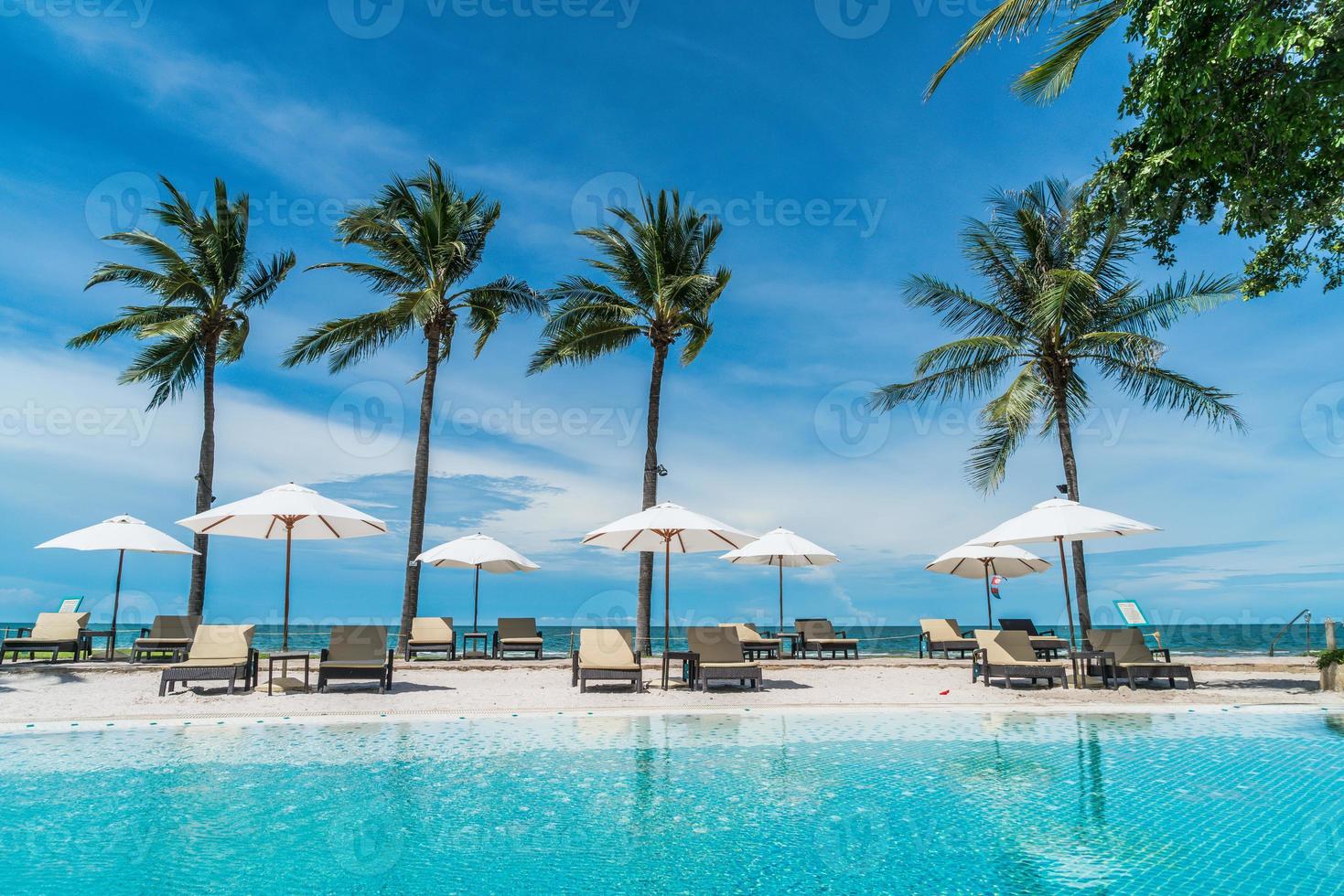 Chair pools or beds and umbrellas around swimming pool with sea background - Holidays and vacation concept photo