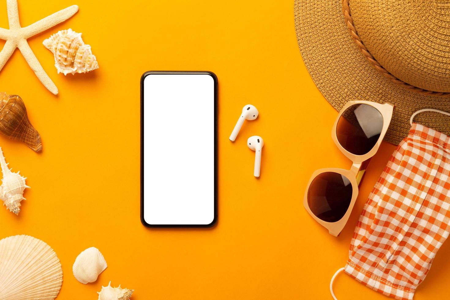 Summer background with blank screen phone and beach accessories, mask to prevent covid-19 on vibrant orange background top view with copy space. photo