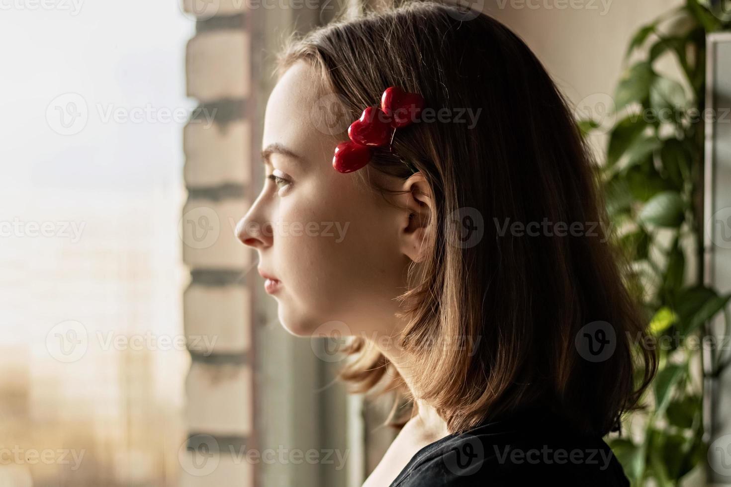 retrato de una hermosa niña triste mirando por la ventana con esperanza y expectativa. horquilla con corazones. primer amor en el dia de san valentin foto