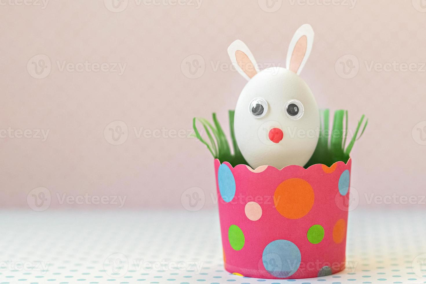 huevo de gallina blanco con orejas de conejo y bozal en una bandeja de papel rosa ecológico, caja. feliz concepto de vacaciones de pascua. foto