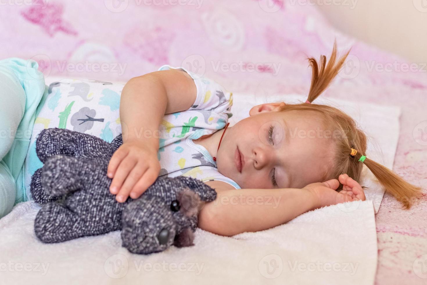 A little girl toddler is sleeping on a bed with toys cuddled . Childhood. photo