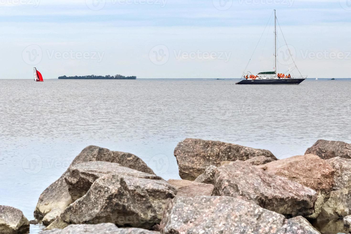 Granite stones in the water on the shore of the Gulf of Finland. Sailboats float on the water photo