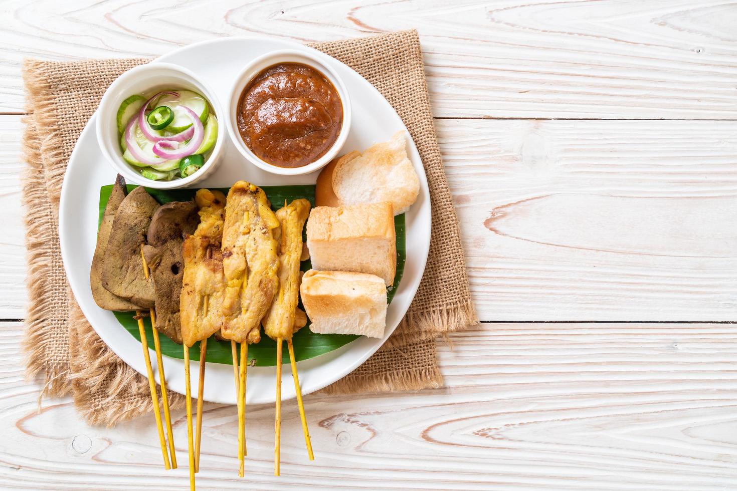 satay de cerdo con tu salsa de maní y encurtidos que son rodajas de pepino y cebolla en vinagre foto