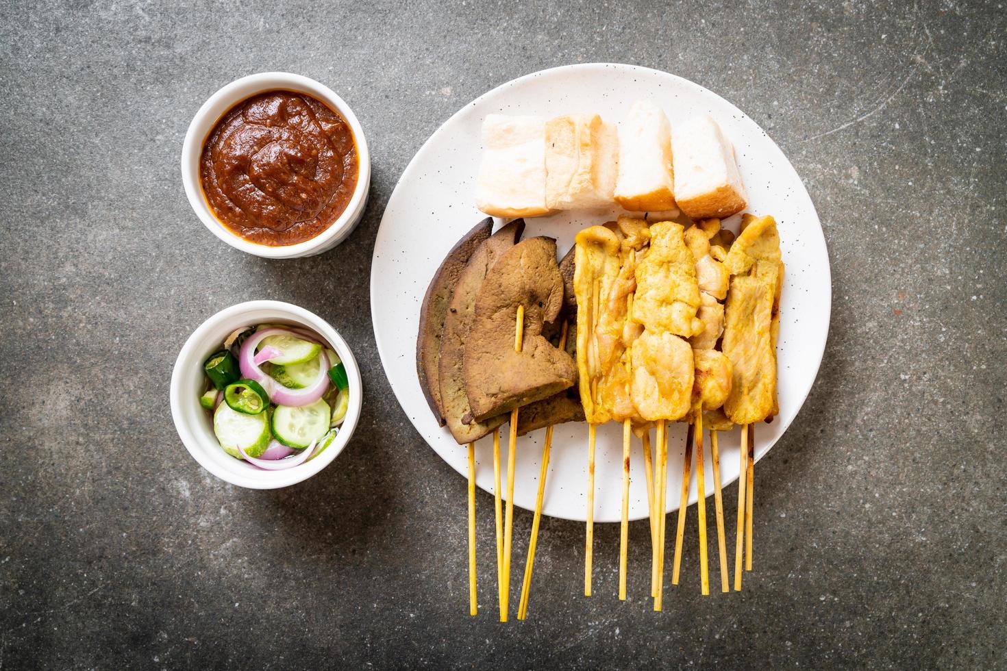 satay de cerdo con tu salsa de maní y encurtidos que son rodajas de pepino y cebolla en vinagre foto