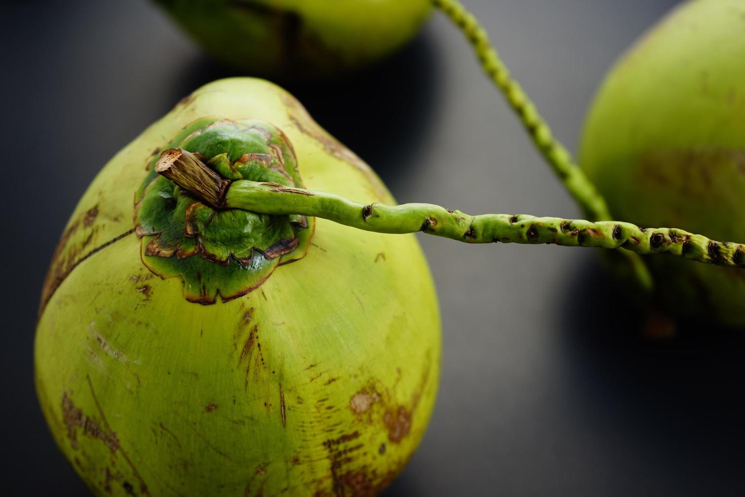 grupo, pila de cocos crudos verdes frescos de plantación plana yacía sobre fondo abstracto de textura negra. comida, concepto de naturaleza muerta con fotografía oscura. foto