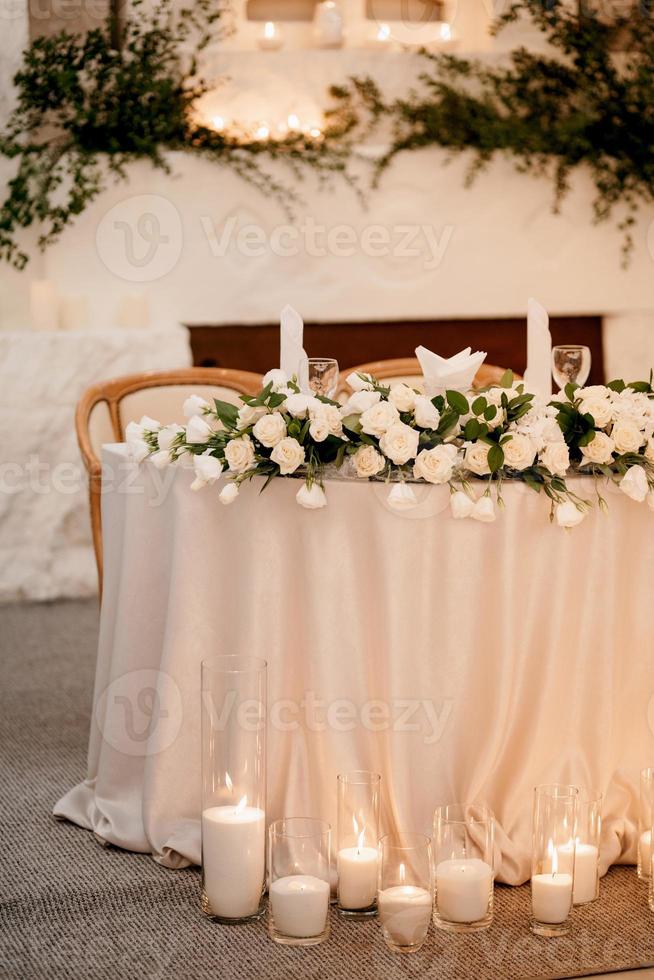 el presidium de los recién casados en el salón de banquetes del restaurante está decorado con velas y plantas verdes foto