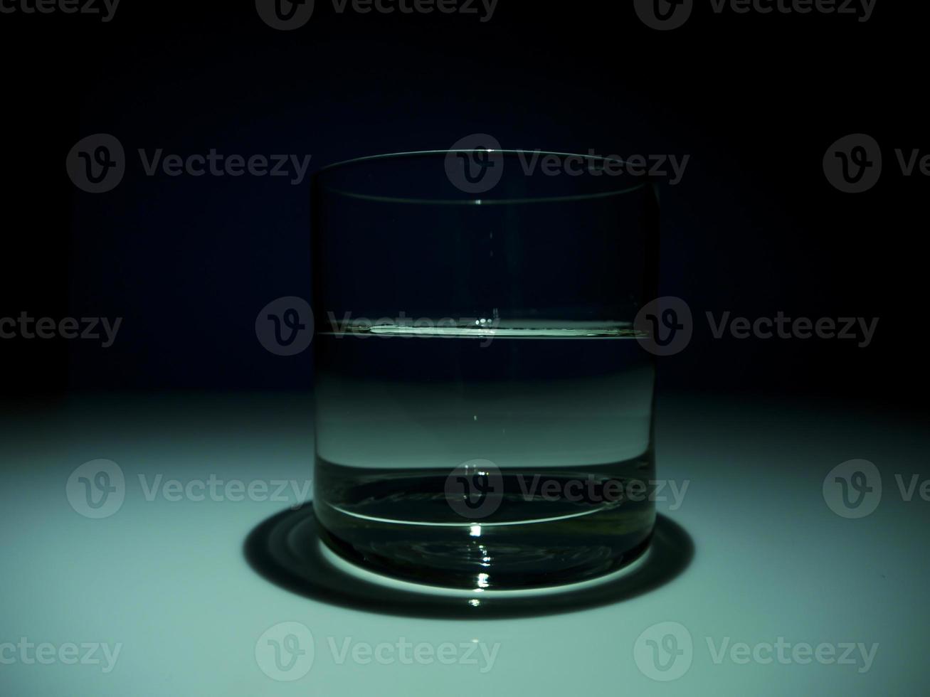 medio vaso lleno con agua en la oscuridad. fondo negro foto