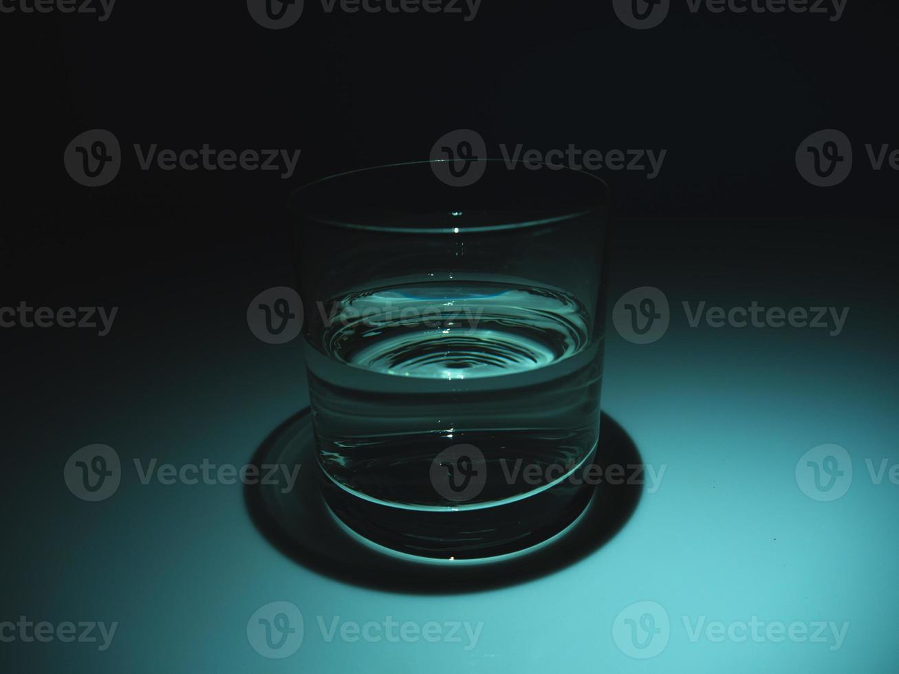 Half full glass with water on the dark. Black background photo