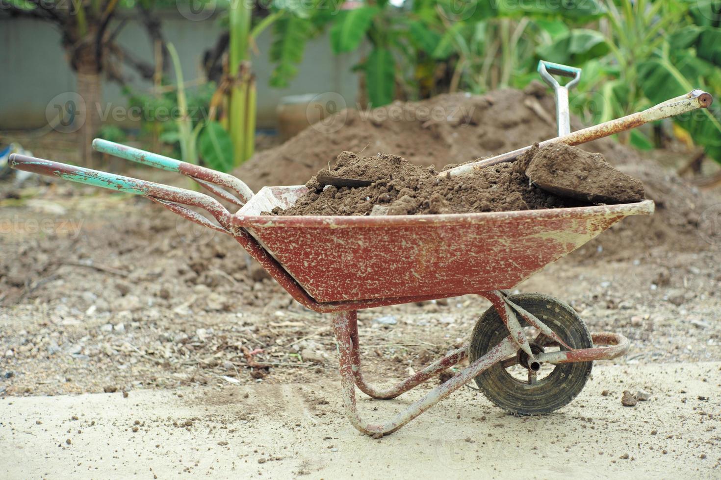 Closeup steel cart carrying the soil with shovels with blurred pile of soil and landscape in background photo