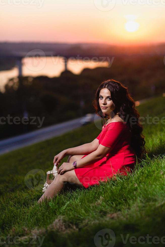 Hermosa joven sentada en una pendiente cubierta de pasto verde foto
