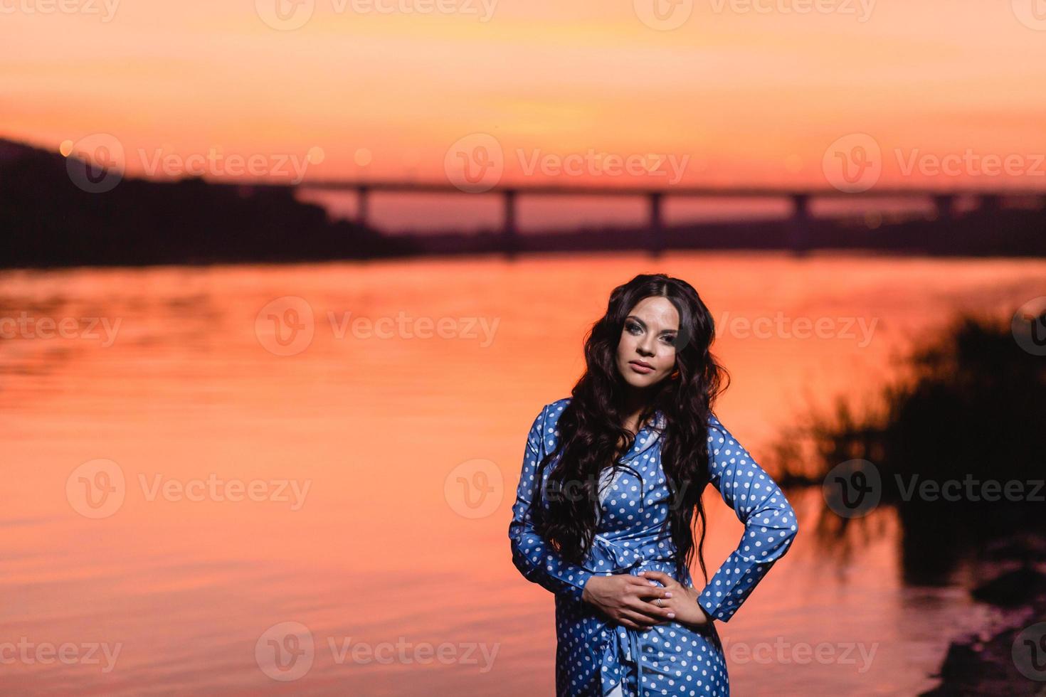 Hermosa joven con largo cabello ondulado oscuro de pie en la orilla del río foto