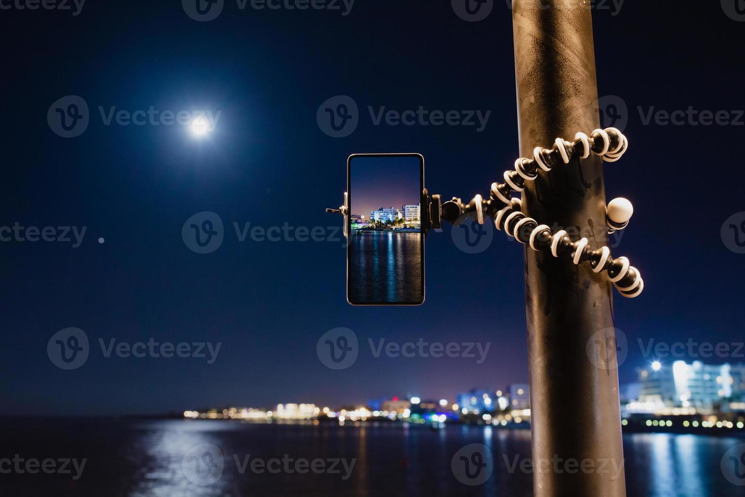 usando un teléfono inteligente en un trípode plegable con larga exposición al mar por la noche foto