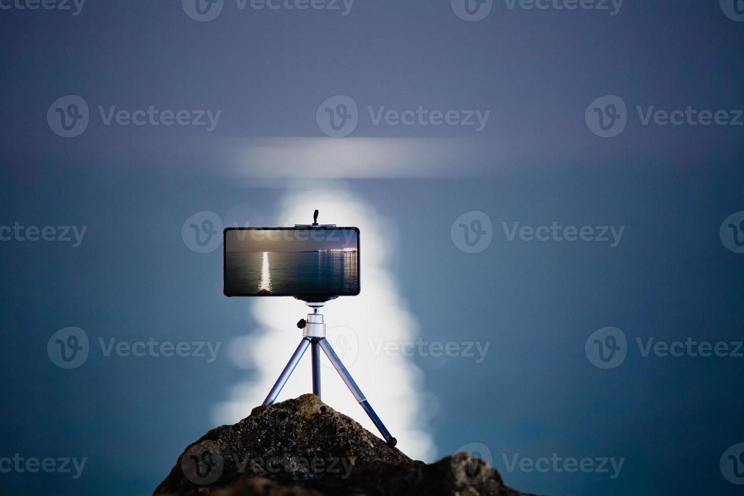 usando un teléfono inteligente en un trípode con larga exposición al mar por la noche foto