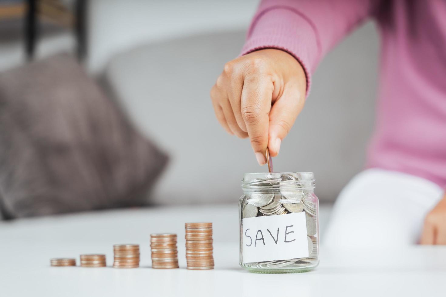 Mano de mujer poniendo moneda de dinero en frasco de vidrio para ahorrar dinero. Ahorro de dinero y concepto financiero. foto