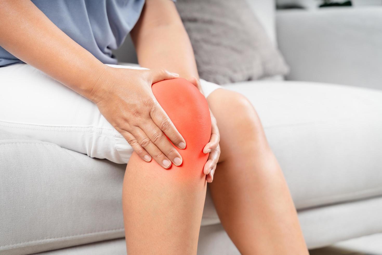 Close up of chubby woman sitting on the sofa and feeling knee pain and she massages her knee. Healthcare and medical concept. photo