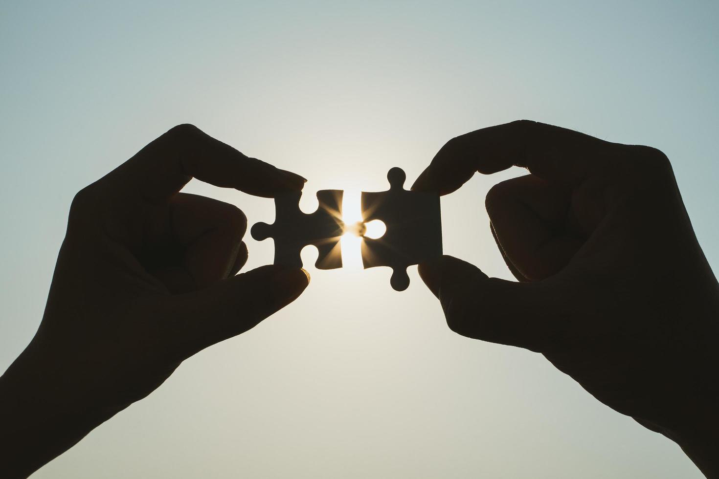 Silhouette of closeup woman and man hand connecting a piece of jigsaw puzzle over sunlight effect. symbol of association and connection concept. business strategy. photo