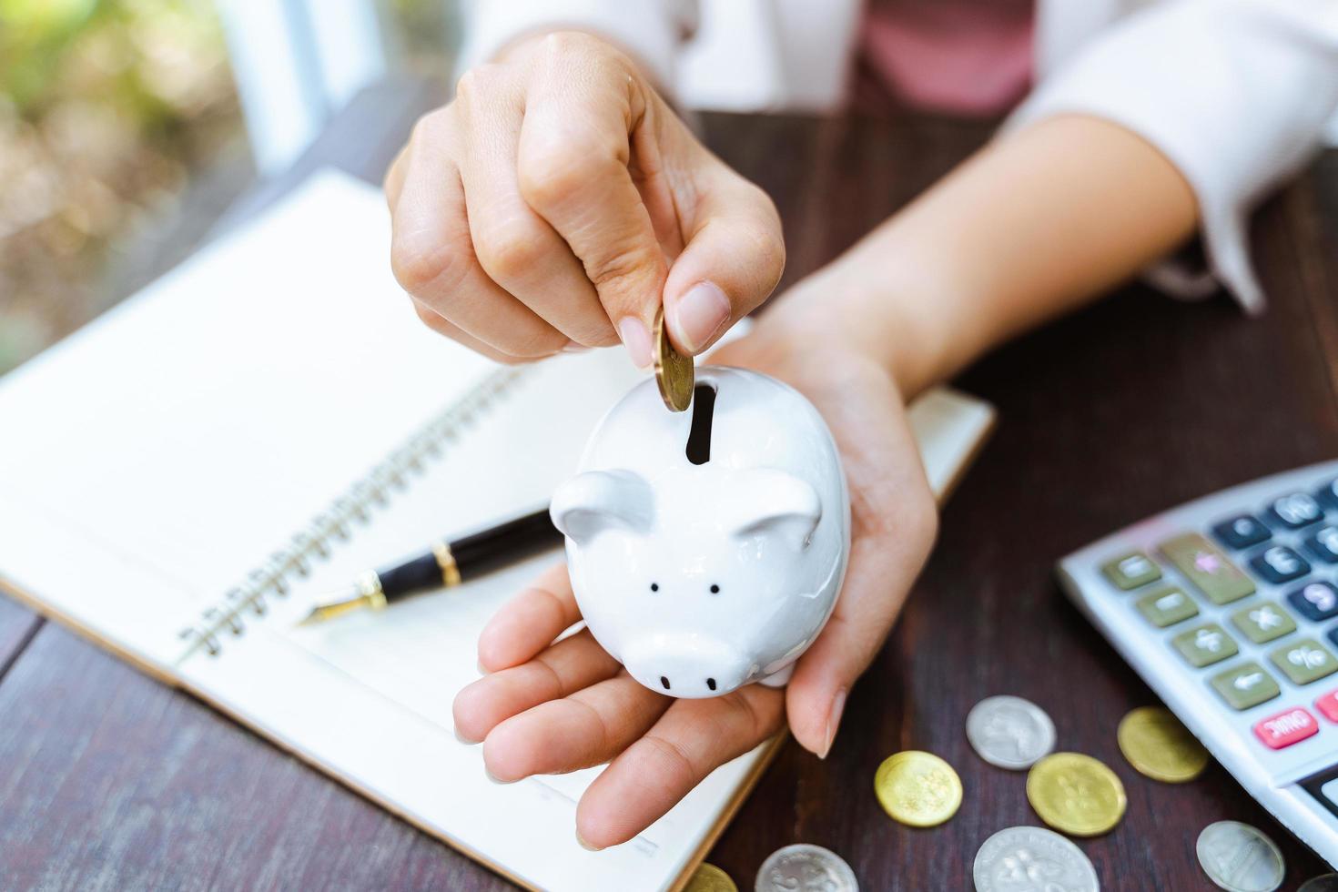 Primer plano de la mano de la mujer de negocios poniendo moneda de dinero en la hucha para ahorrar dinero. Ahorro de dinero y concepto financiero. foto