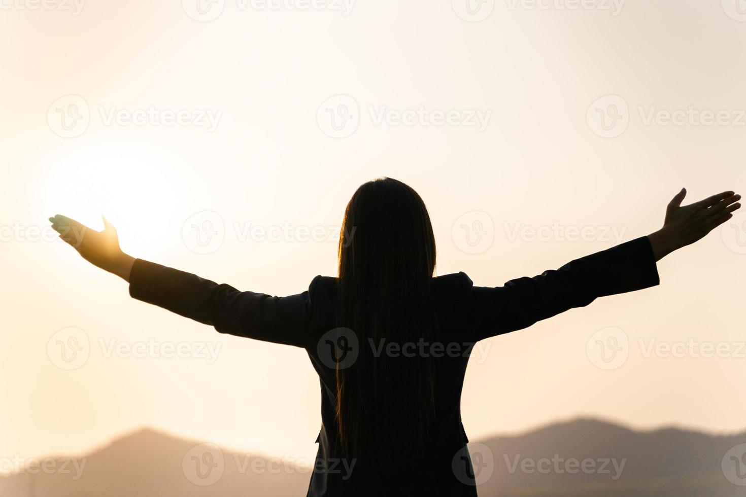 feliz empresaria extendiendo los brazos y mirando la silueta de la montaña. concepto de éxito empresarial, emociones de libertad foto