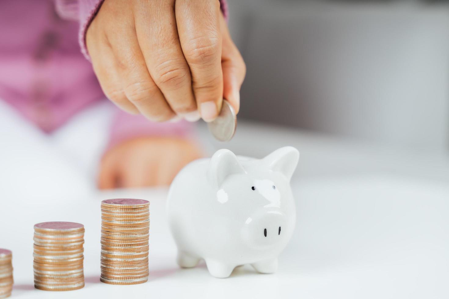 Primer plano de la mano de la mujer de negocios poniendo moneda de dinero en la hucha para ahorrar dinero. Ahorro de dinero y concepto financiero. foto