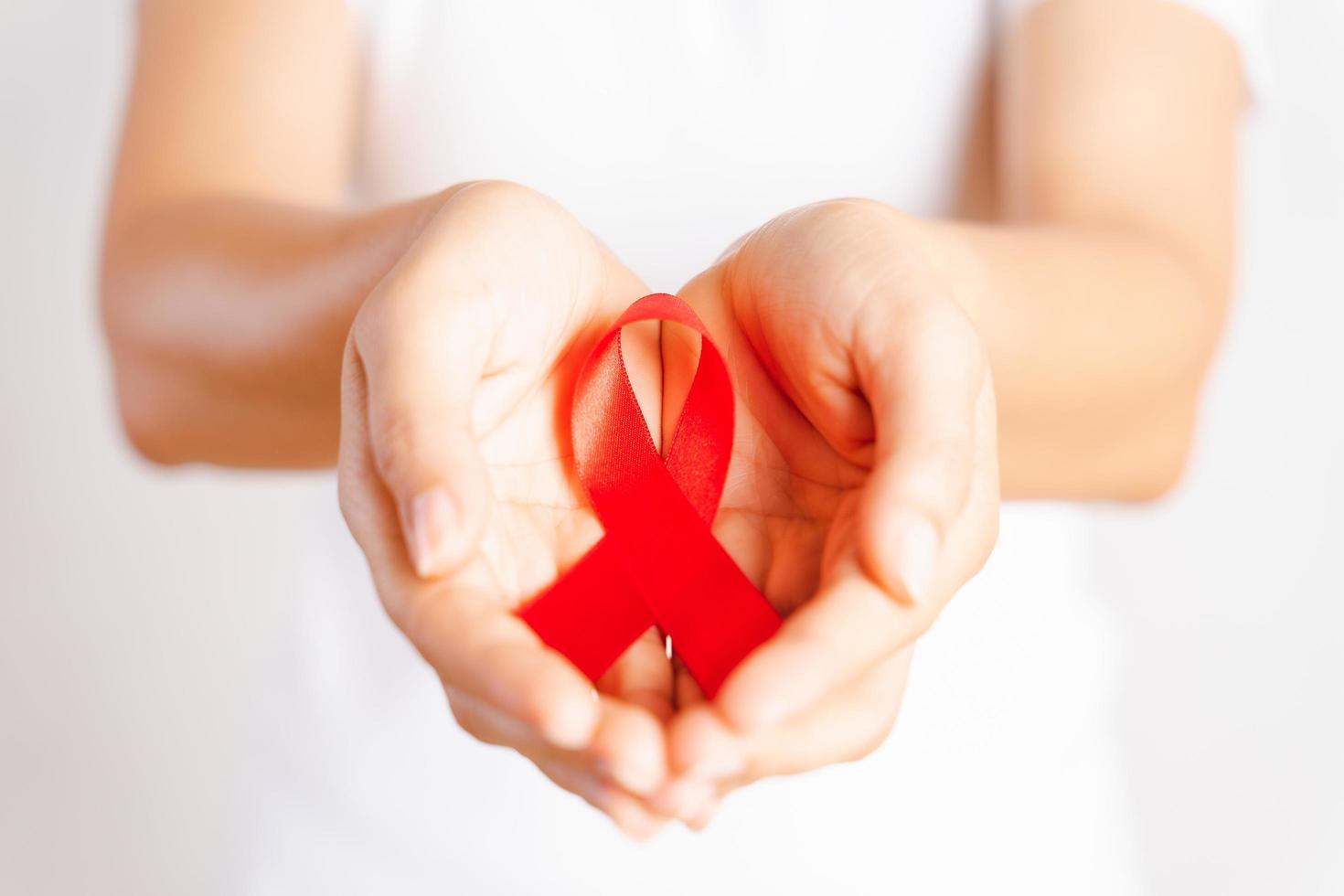 Closeup woman hand holding red ribbon HIV, world AIDS day awareness ribbon. Healthcare and medicine concept. photo