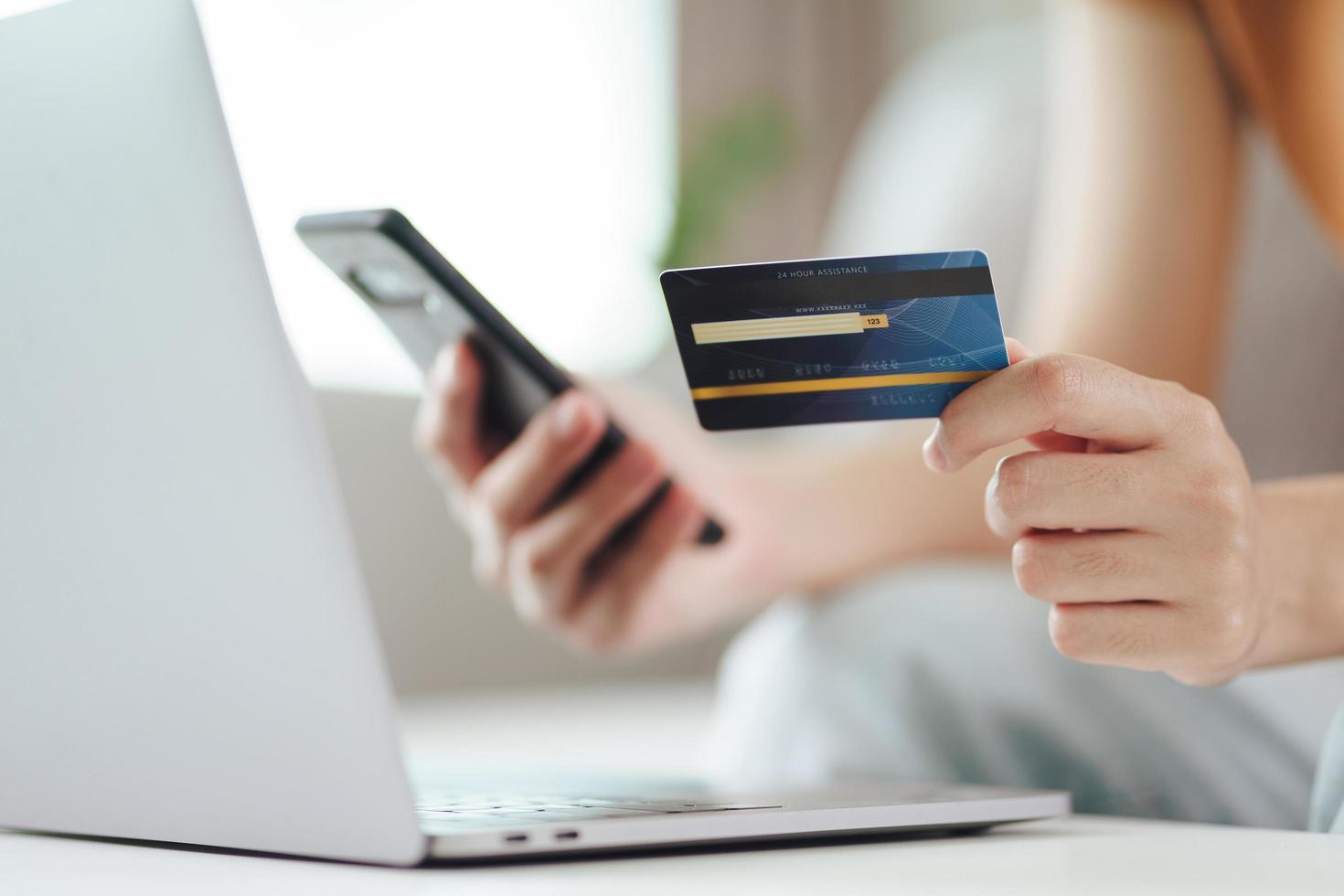 Mujer joven con tarjeta de crédito y uso de teléfonos inteligentes para compras en línea, banca por Internet, comercio electrónico, gastar dinero, trabajar desde el concepto de hogar foto