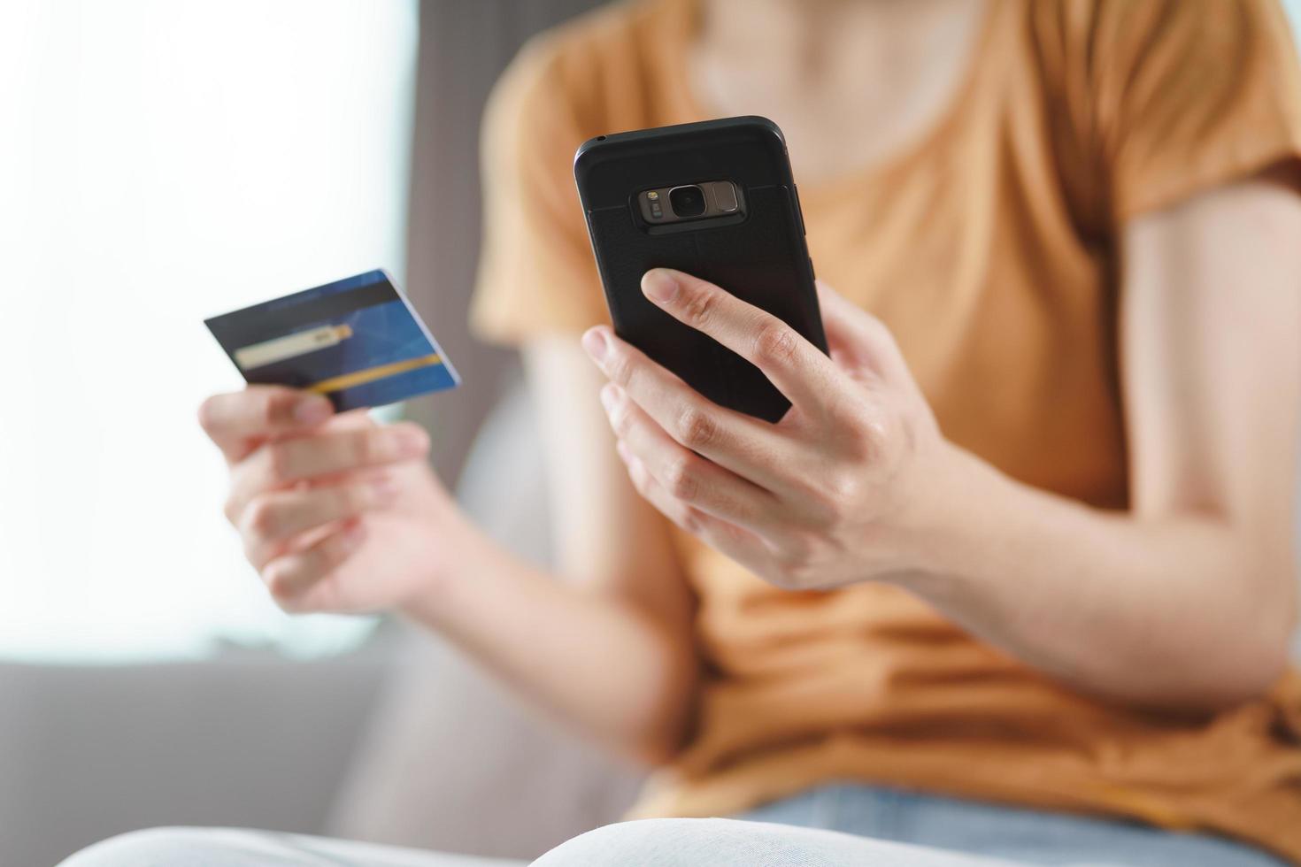 Young woman holding credit card and using smart phone for online shopping, internet banking, e-commerce, spending money, working from home concept photo