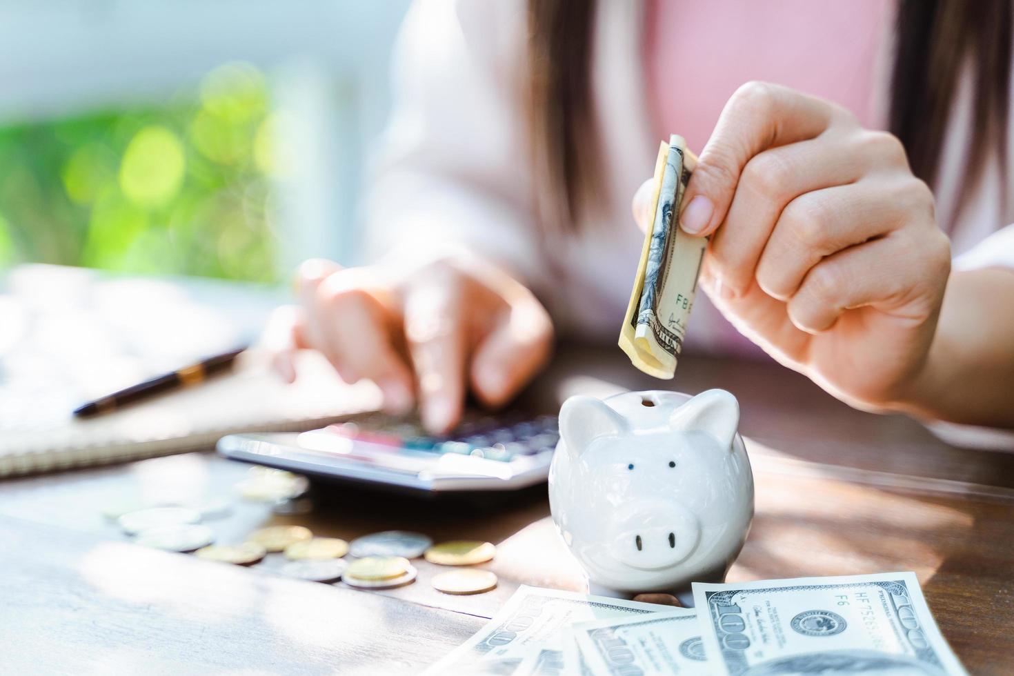 Primer plano de la mano de la mujer de negocios poniendo moneda de dinero en la hucha para ahorrar dinero. Ahorro de dinero y concepto financiero. foto