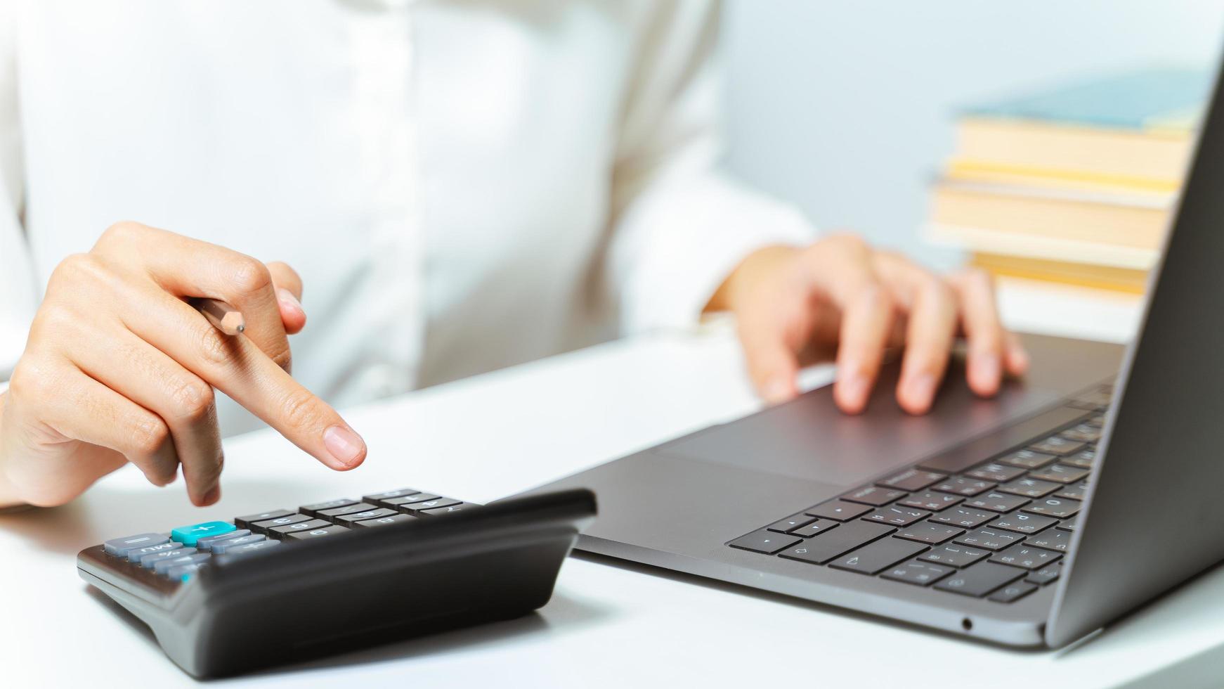 Close up of woman hand using calculator and computer laptop in home or office. photo