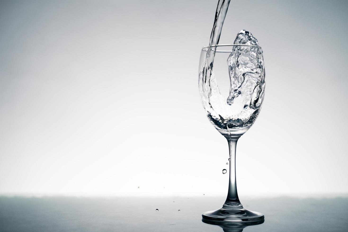 Close up of splash of crystal clear water pouring into the wine glass on the table. photo