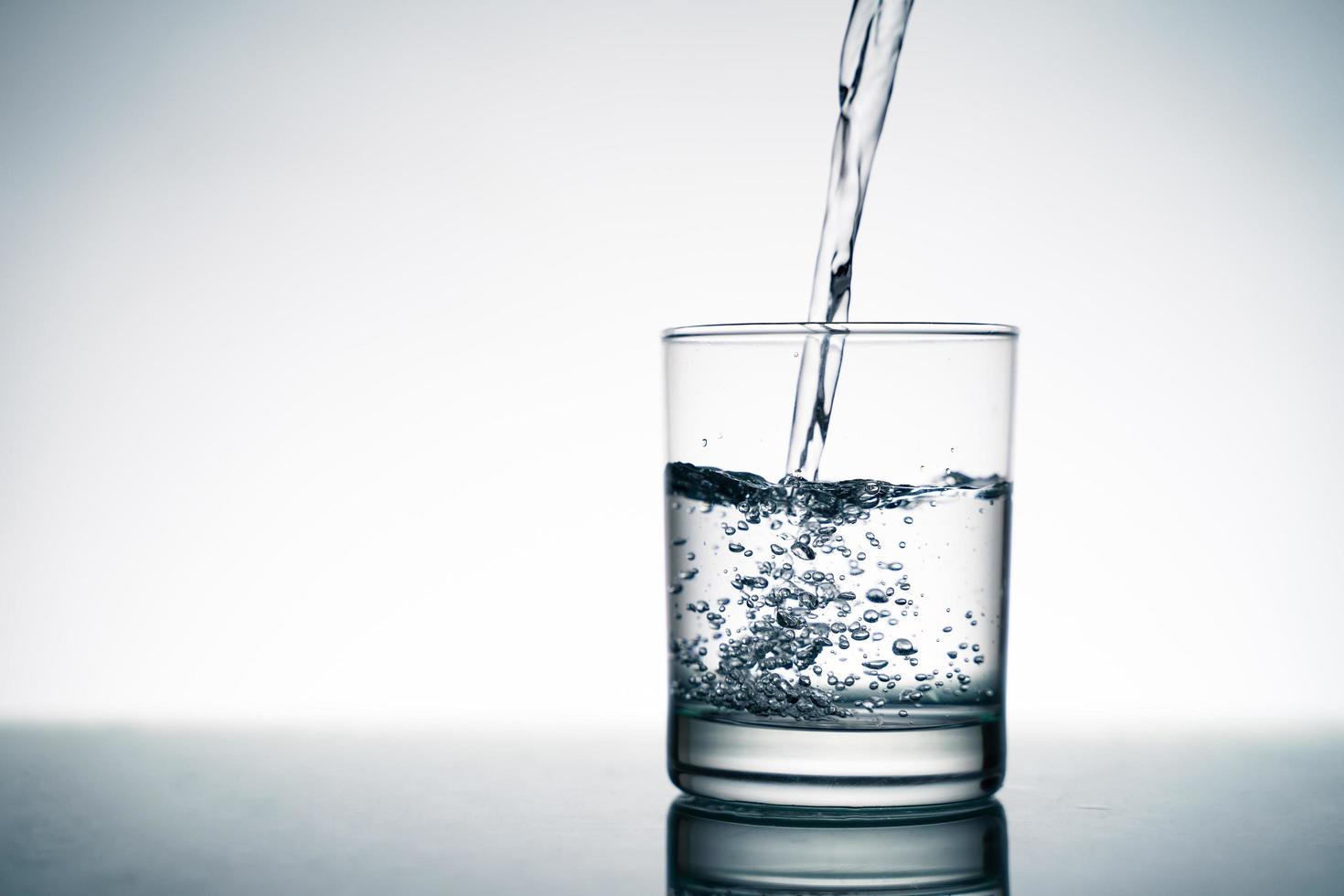 Cerca de verter agua fresca en el vaso transparente de la botella en la mesa. foto