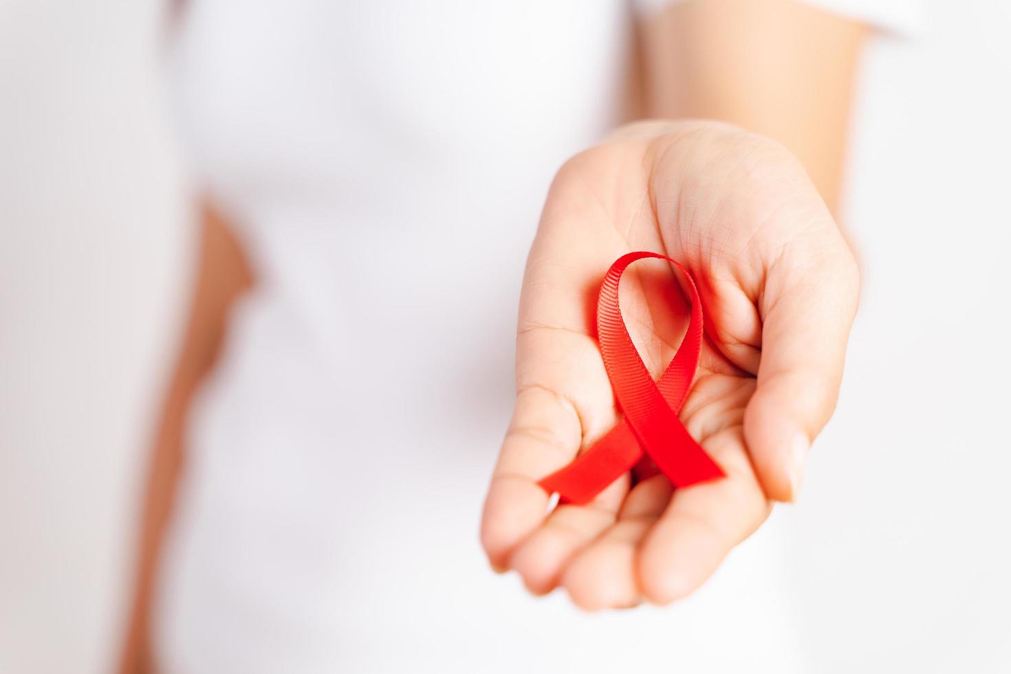 Closeup woman hand holding red ribbon HIV, world AIDS day awareness ribbon. Healthcare and medicine concept. photo