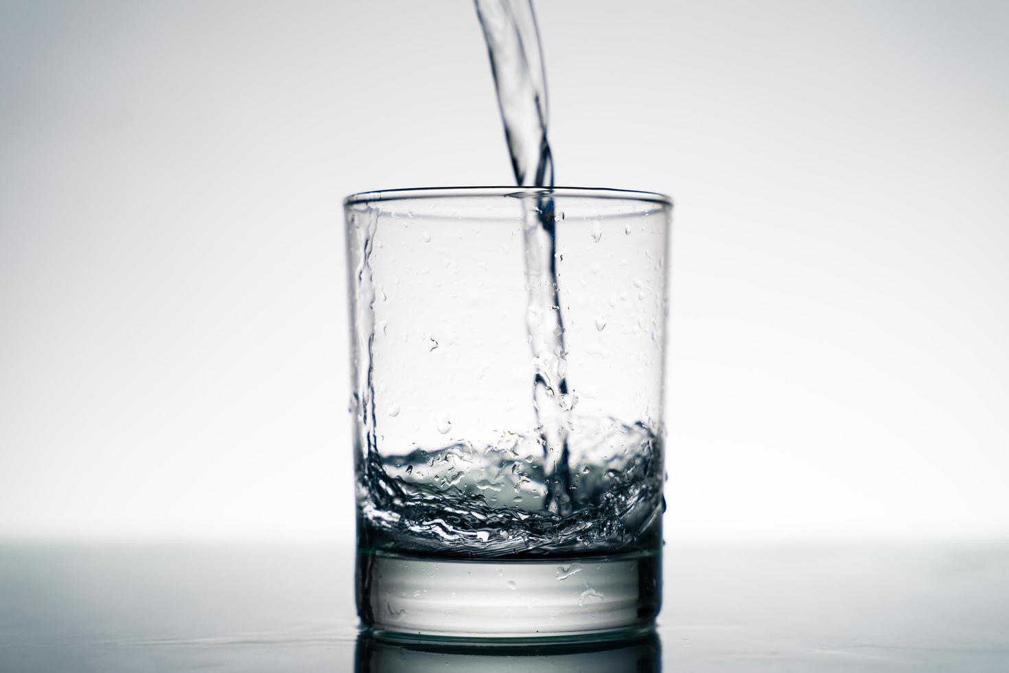 Close up of pouring fresh water into the clear glass from the bottle on table. photo