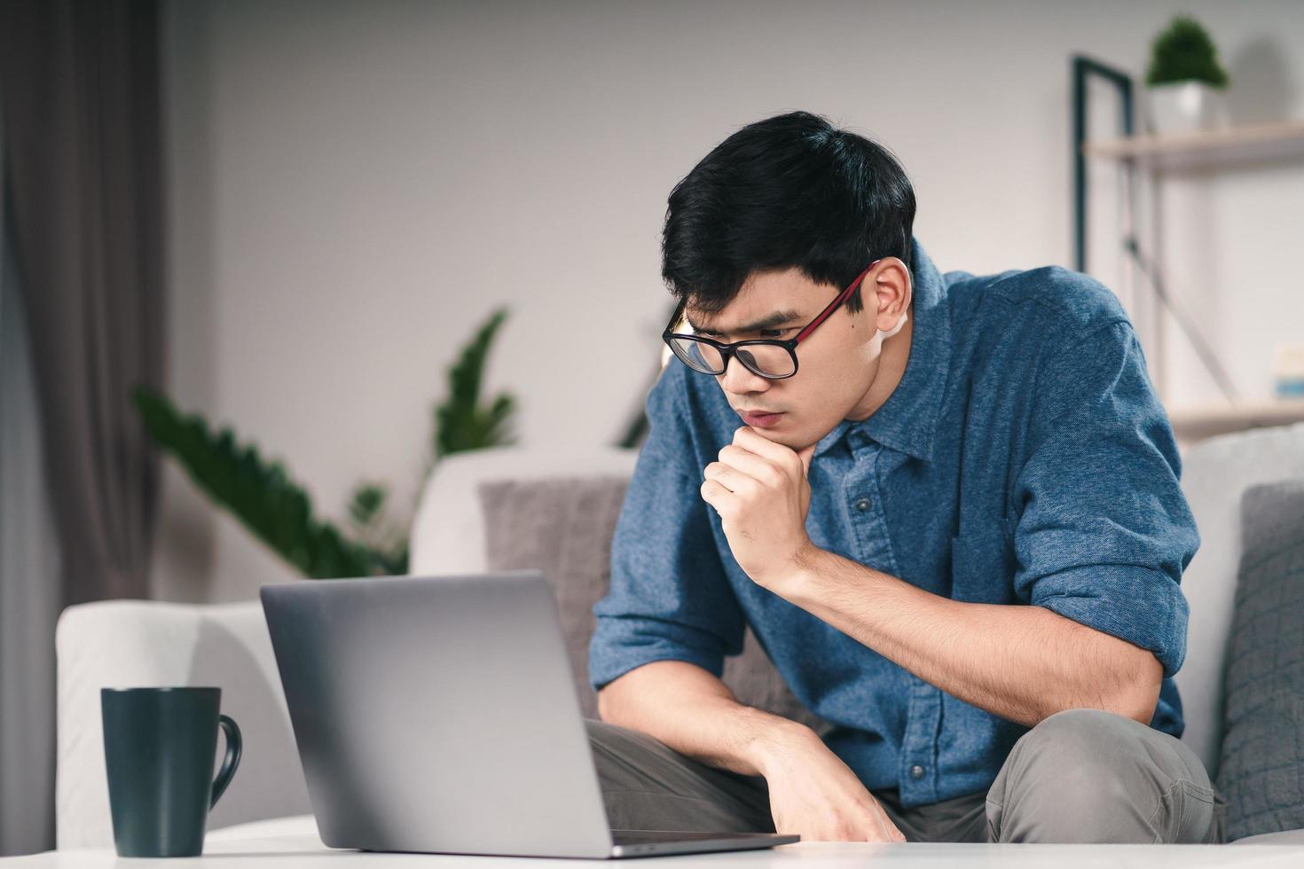 Hombre asiático serio pensativo pensativo en anteojos mirando la pantalla del portátil pensando en una solución para resolver el problema. foto
