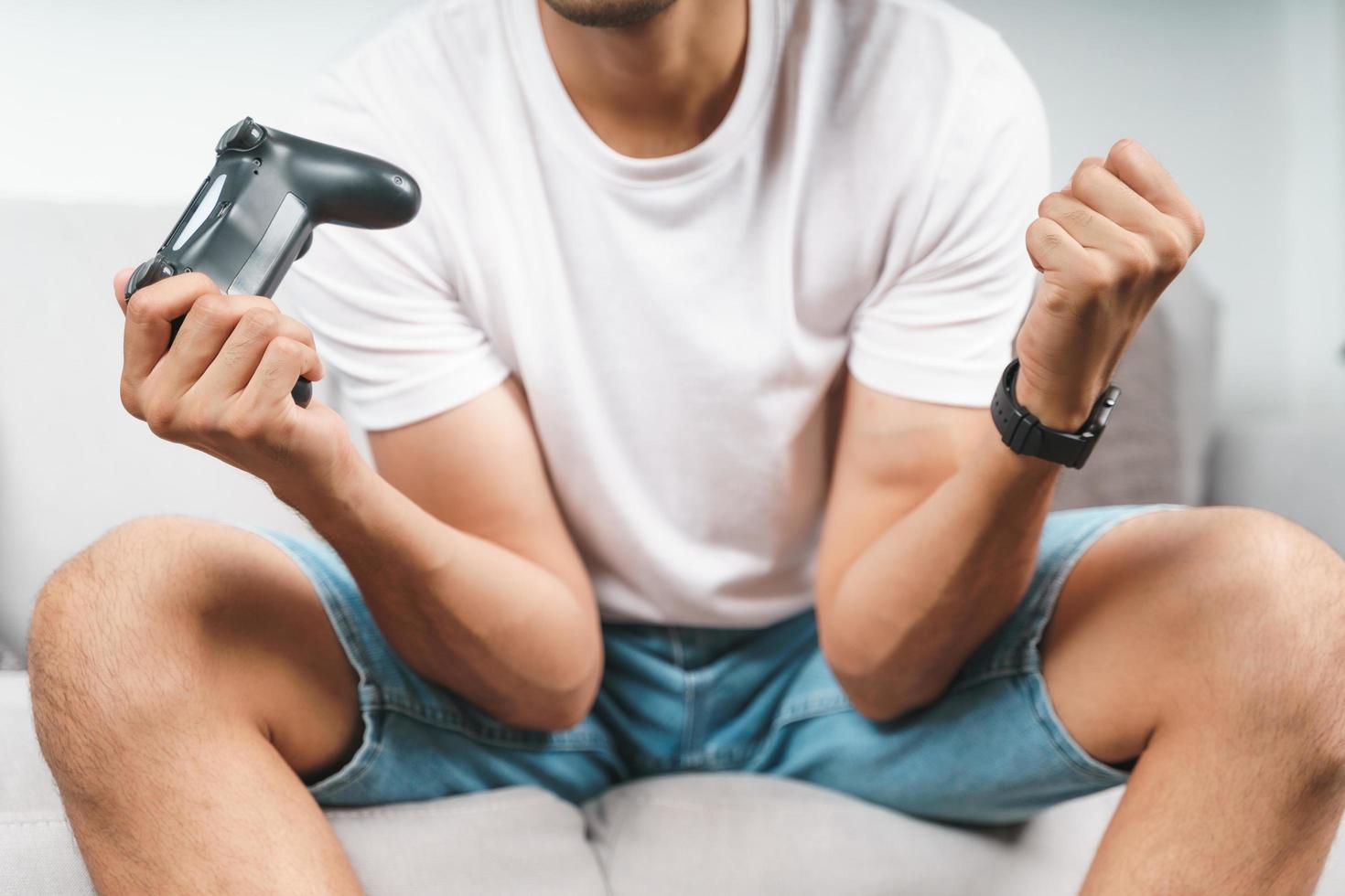 Excited young handsome man playing video game and raising fists sitting on the couch at home. photo