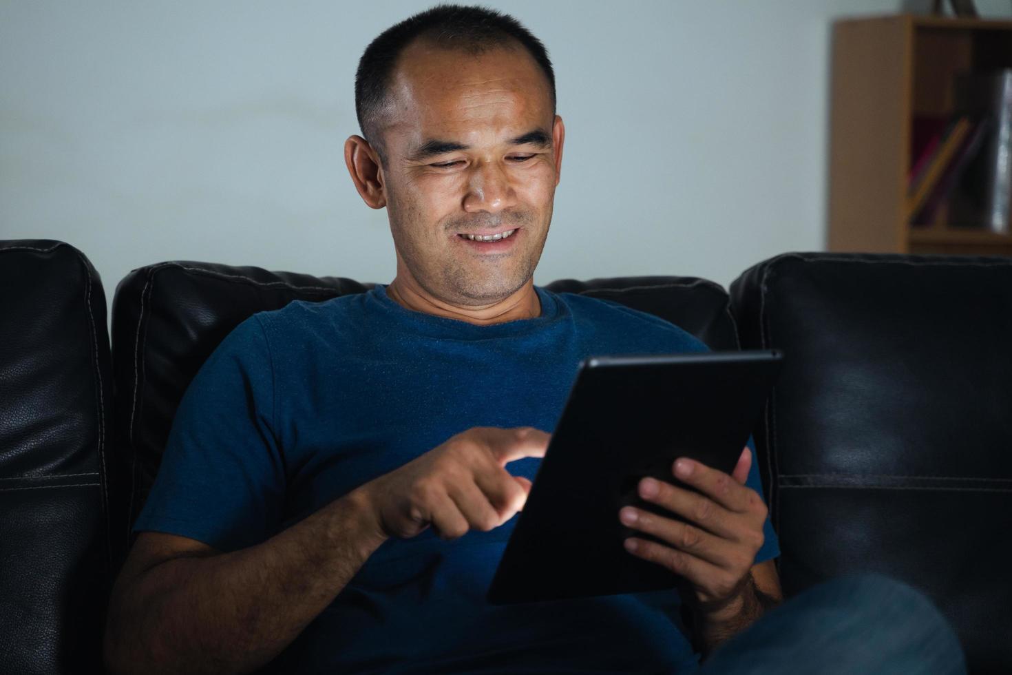 hombre sentado en el sofá, usando la tableta para trabajar o relajarse en casa. trabajar desde el concepto de hogar. foto