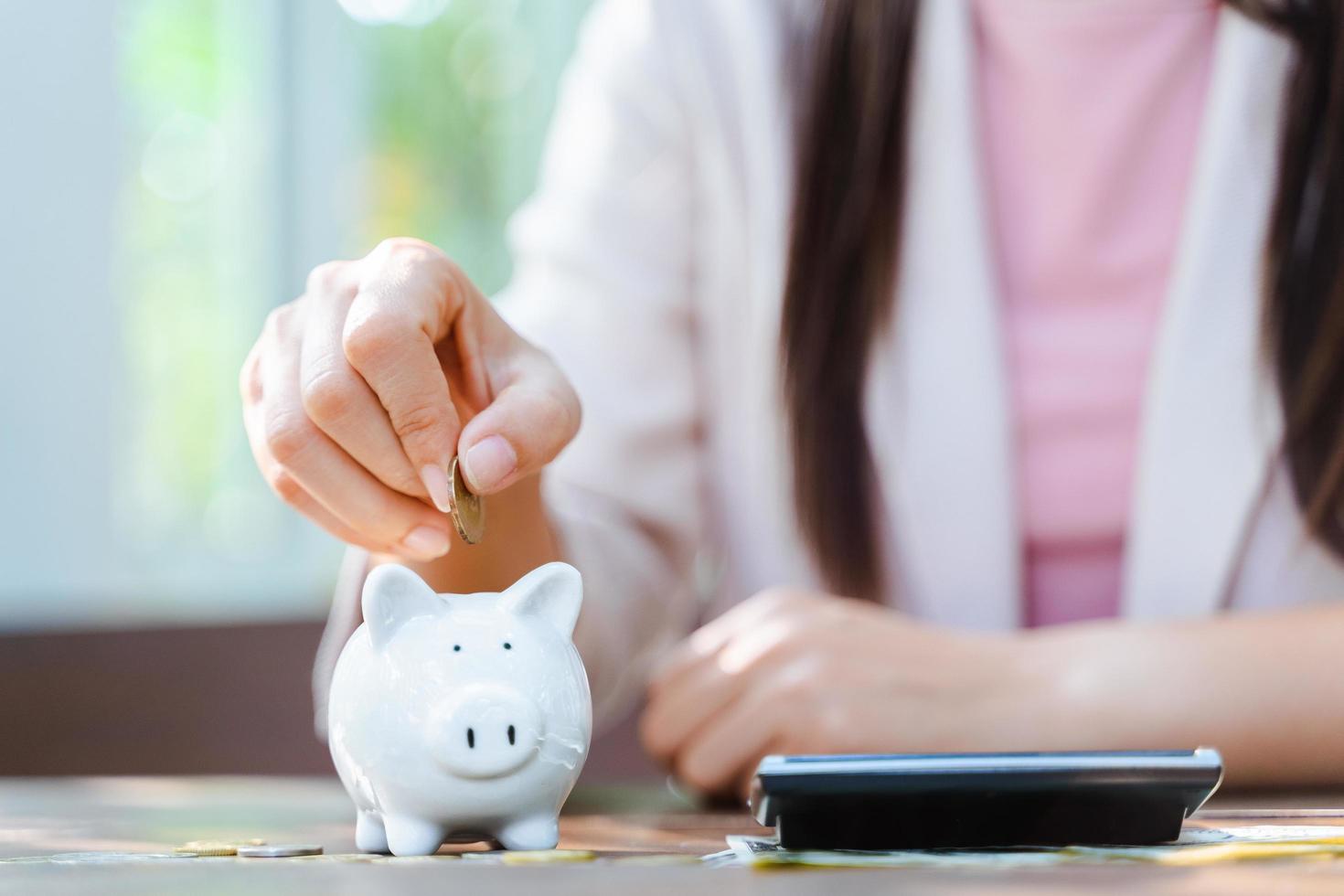 Primer plano de la mano de la mujer de negocios poniendo moneda de dinero en la hucha para ahorrar dinero. Ahorro de dinero y concepto financiero. foto