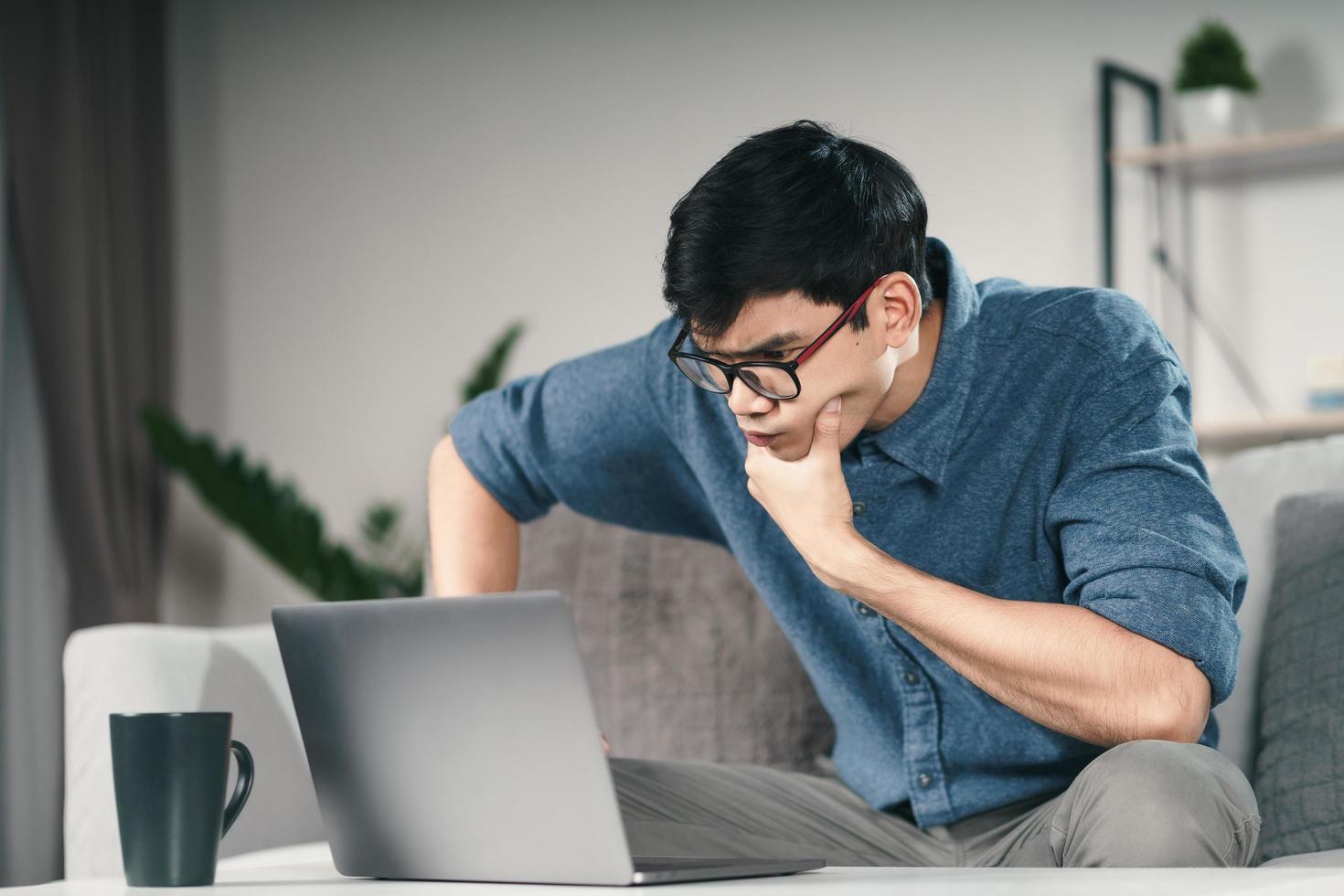 Pensive Thoughtful Serious Asian man in eyeglasses looking at laptop screen thinking for solution to solve the problem. photo