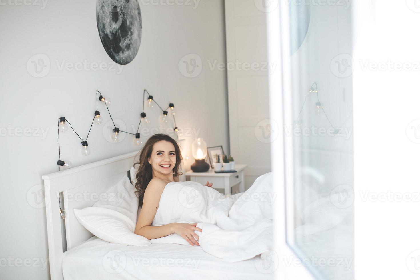 hermosa mujer joven que se despierta en una cómoda cama en sábanas blancas frescas. foto