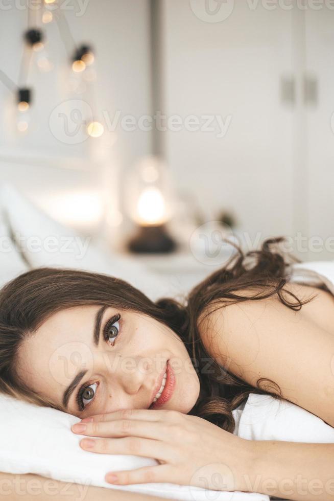 Beautiful young woman waking up in comfortable bed on white fresh sheets. photo