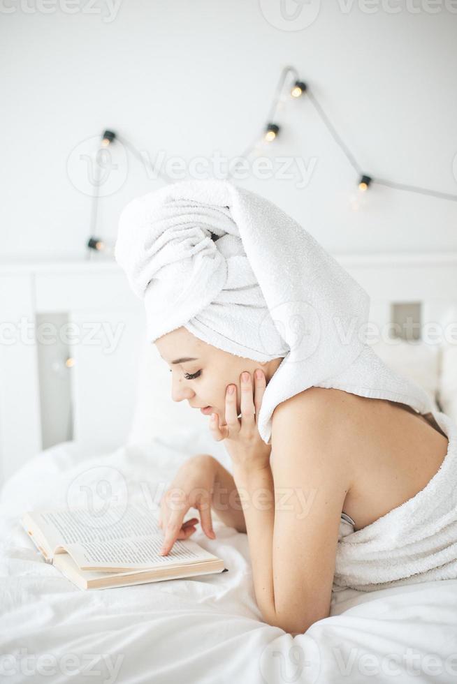 Young happy woman reading paper book in bed. photo