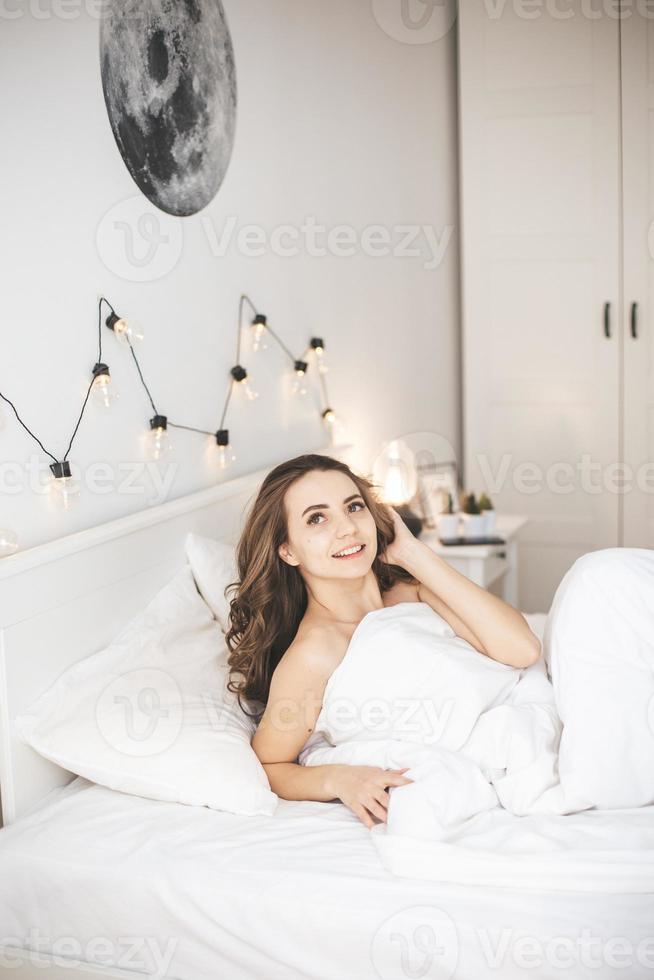 hermosa mujer joven que se despierta en una cómoda cama en sábanas blancas frescas. foto