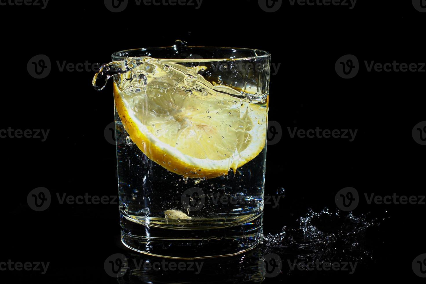 agua con limón en un vaso sobre un fondo negro. foto